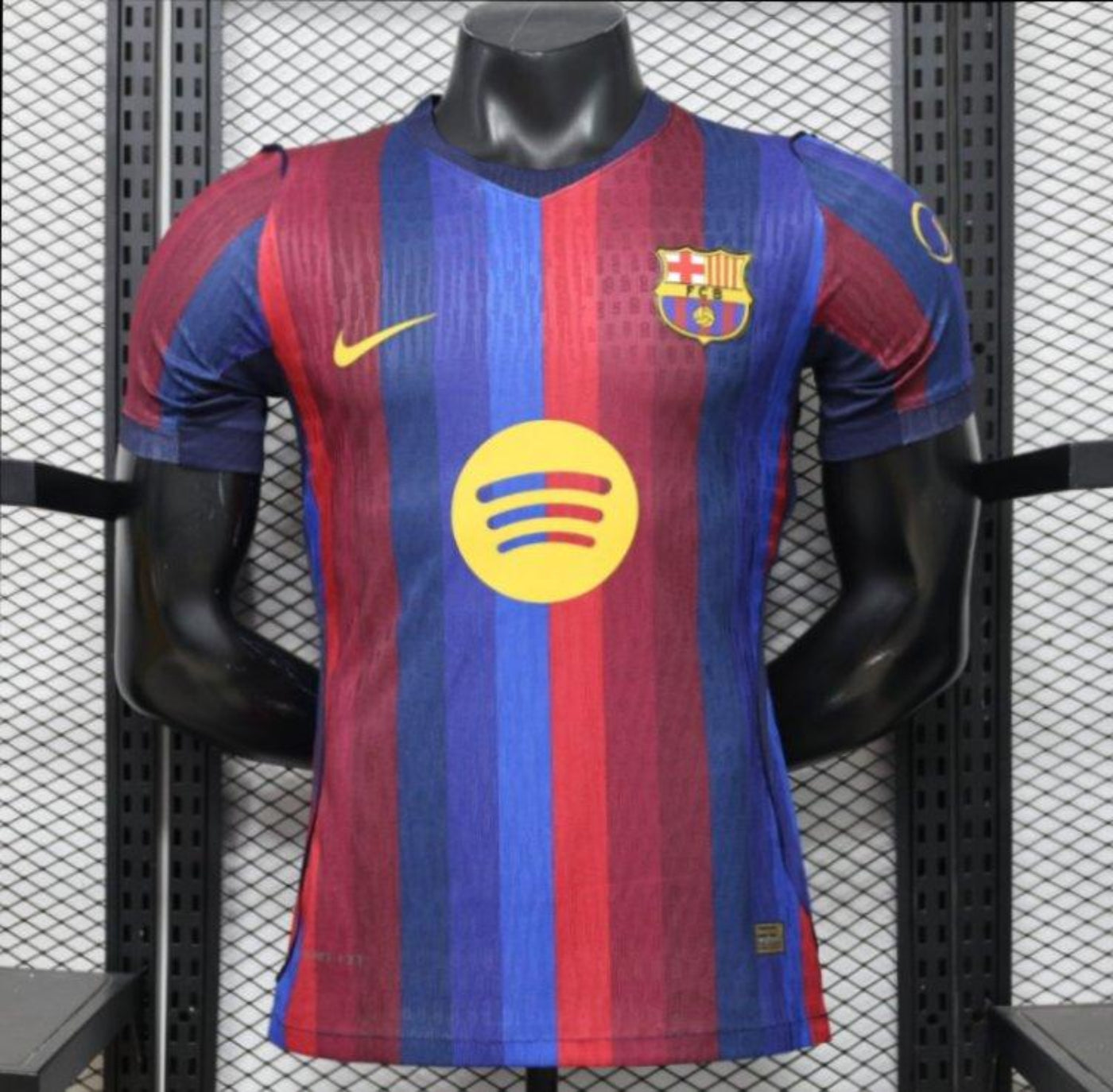 FC Barcelona home soccer jersey with red and blue vertical stripes, featuring a yellow Nike swoosh, FC Barcelona crest, and a yellow Spotify sponsor logo, displayed on a black mannequin torso.