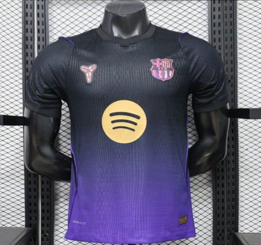 A dark purple and black gradient FC Barcelona soccer jersey with a gold Spotify sponsor logo on the chest, displayed on a black mannequin torso against a gray mesh background.